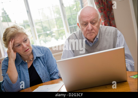 Senior anziana coppia utilizzando un computer portatile, guardando preoccupato Foto Stock