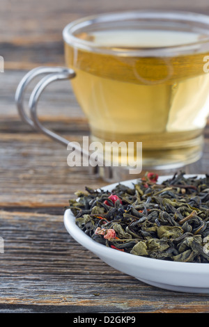 Foglie di tè verde su una piastra di vetro, tazza di tè in background Foto Stock
