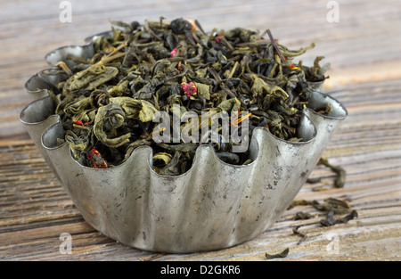 Allentate di foglie di tè verde in una rustica tortina di metallo su sfondo di legno Foto Stock