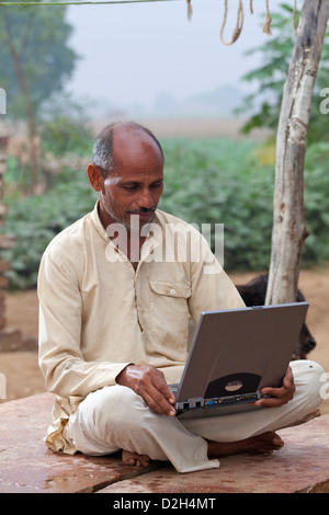 India, Uttar Pradesh, uomo di mezza età guardando il computer portatile nel villaggio rurale di impostazione Foto Stock