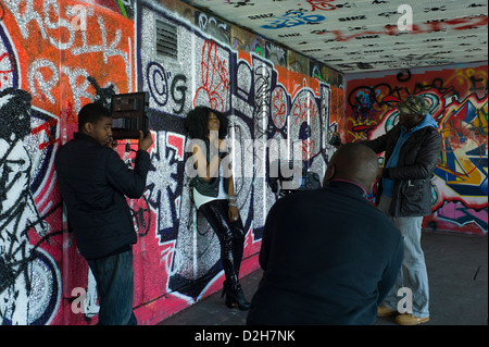 Londra, Southbank, Riverside, Embankment giovane ragazza nera femmina cantante pop riprese video nella parte anteriore del graffiti, arte di strada. Foto Stock