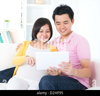 Coppia asiatica. Il marito e 8 mesi moglie incinta utilizzando computer tablet seduti sul divano di casa Foto Stock