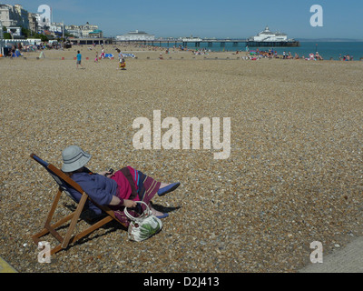 Signora seduta sulla sedia a sdraio con Eastbourne Pier in background, Eastbourne Inghilterra - Agosto 2012 Foto Stock