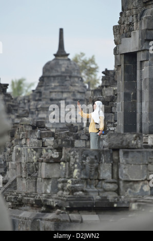 Una velata donna indonesiana a controllare il suo telefono cellulare nel tempio di Candi Sewu a Prambanan; Yogyakarta, Java. Indonesia. Foto Stock