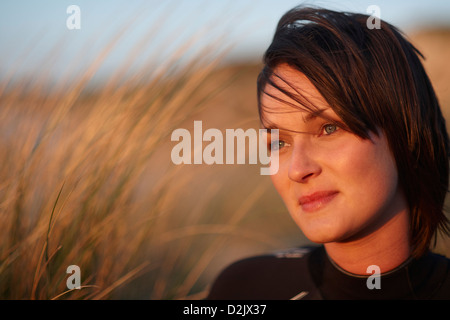 Giovane donna seduta in erba lunga muta da indossare al tramonto / sunrise Foto Stock