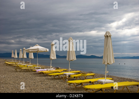 Nuvole scure e vacante sedie a sdraio in spiaggia Foto Stock