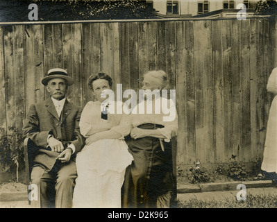Circa 1890 fotografia, genitori anziani e la loro figlia cresciuto squeeze insieme su una panchina del cortile. Foto Stock