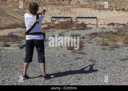 Donna che indossa Protezioni per udito e un gunbelt, puntando una pistola a bersagli in un poligono di tiro Wyoming USA Foto Stock
