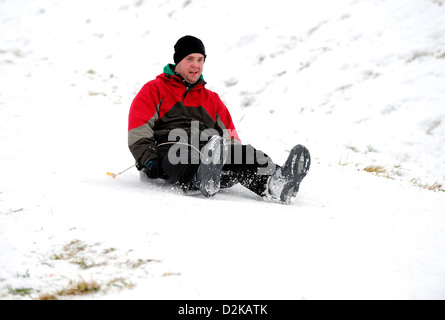 Giovani uomini godendo di slittare verso il basso una coperta di neve collina su un inverni freddi giorno. Foto Stock