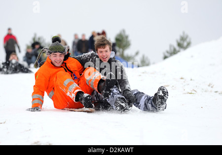 Due giovani uomini godendo lo slittino insieme verso il basso una coperta di neve collina su un inverni freddi giorno. Foto Stock