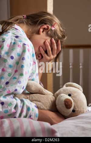 Giovane donna che indossa un pigiama che stringe la Teddy bear, mano che copre il volto. Foto Stock