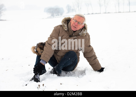 Senior infelice uomo con ferite dolorose gamba sulla neve. Foto Stock