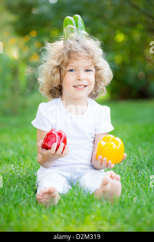 Sorridenti bambino con verdure seduto su erba verde nella primavera del parco. Uno stile di vita sano concetto Foto Stock