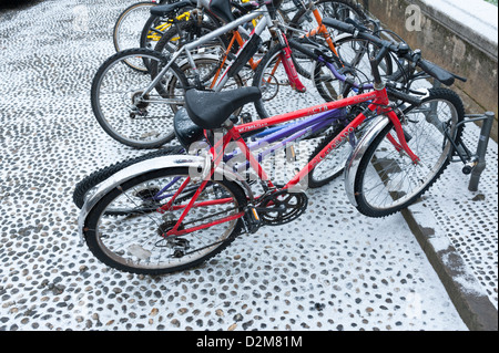 Cicli parcheggiato su ciottoli in Cambridge Regno Unito nella neve. Foto Stock