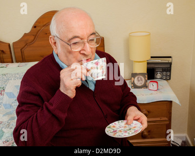 Anziani uomo seduto in camera da letto bicchiere di tè Foto Stock