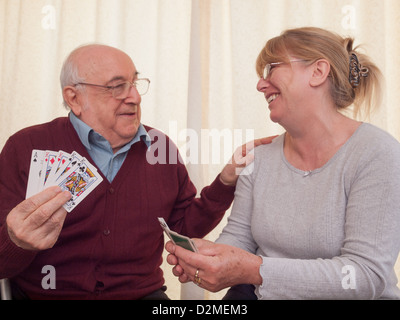 Uomo anziano giocando a carte con la figlia e ridere Foto Stock