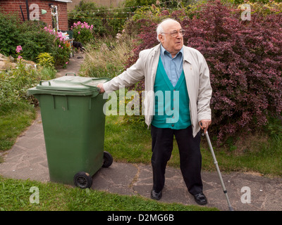 Uomo anziano tirando il verde bidone con ruote lungo il percorso del giardino Foto Stock