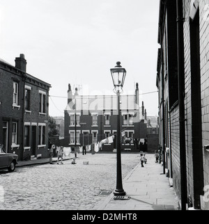 Lampada da strada a gas e lavanderia pensile madre su una linea di lavaggio in una vecchia strada acciottolata con case a schiera vittoriana e bambini che giocano a giochi in 1970s anni settanta 70s Wolseley Grove Leeds Inghilterra Regno Unito Gran Bretagna 1974 KATHY DEWITT Foto Stock