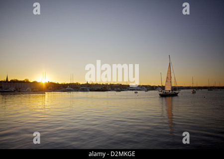 Sereno tramonto in barca a vela nel Rhode Island, catturando una barca a vela che naviga attraverso acque tranquille sullo sfondo di un pittoresco skyline costiero Foto Stock