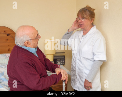 Accompagnatore a parlare con persone anziane signore di circa problemi uditivi seduto sul letto Foto Stock