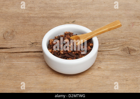 Chiodi di garofano interi in un ramekin con un cucchiaio di legno su uno sfondo di legno stagionato. Foto Stock