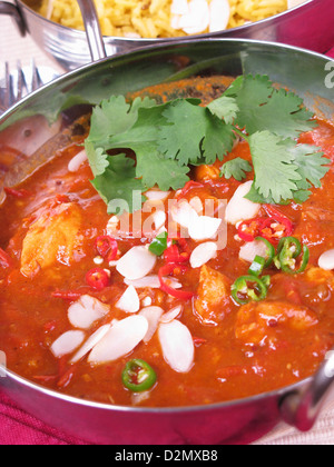 Una ciotola di Goan vindaloo di pollo condito con mandorle a fette tagliate a fette peperoncini e il coriandolo fresco (il coriandolo). Riso allo zafferano dietro. Foto Stock