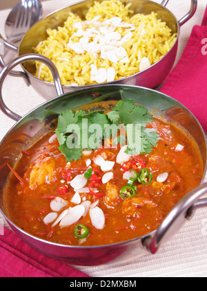 Una ciotola di Goan vindaloo di pollo condito con mandorle a fette tagliate a fette peperoncini e il coriandolo fresco (il coriandolo). Riso allo zafferano dietro. Foto Stock