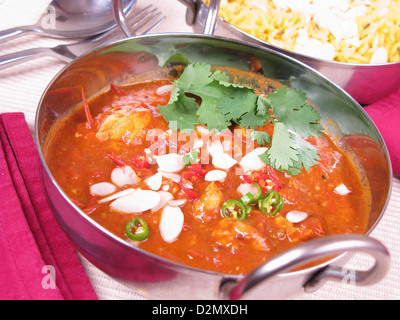 Una ciotola di Goan vindaloo di pollo condito con mandorle a fette tagliate a fette peperoncini e il coriandolo fresco (il coriandolo). Riso allo zafferano dietro. Foto Stock