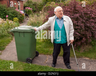 Uomo anziano tirando il verde bidone con ruote lungo il percorso del giardino Foto Stock