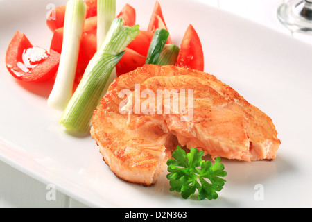 Panoramica di salmone fritto servito con pomodoro e cipolla a molla Foto Stock