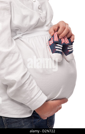 Donna incinta mantenendo baby-scarpe. Immagine ravvicinata di pancia e scarpe. Foto Stock