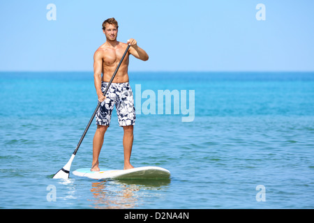 Giovane uomo caucasico felice in piedi sulla tavola da surf paddling sulla spiaggia hawaiana d'estate vacanze viaggi Foto Stock