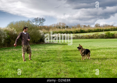 L'uomo circa a buttare in rosso di un anello di gomma giocattolo per pastore tedesco cane nel campo erboso in Bristol con il cane si fermò in attesa Foto Stock