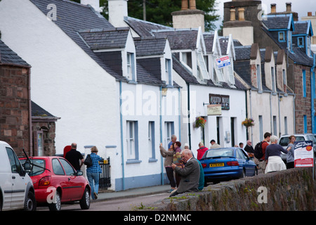 Due uomini seduti su una parete e chat di casette a schiera sul fronte strada di Plockton, un pittoresco villaggio nelle Highlands Scozzesi. Foto Stock