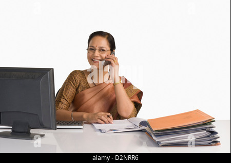 Imprenditrice seduto alla scrivania e a parlare su un telefono mobile Foto Stock