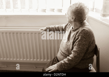 Donna di novanta anni con mano sul radiatore che guarda fuori dalla finestra, Regno Unito. Coronavirus, autoisolamento, distanza sociale, quarantena... concetto Foto Stock