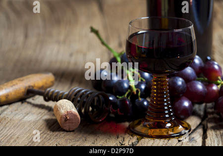 Un bicchiere di vino rosso con bottiglia e uva sono su un vecchio rustico tavolo in legno Foto Stock