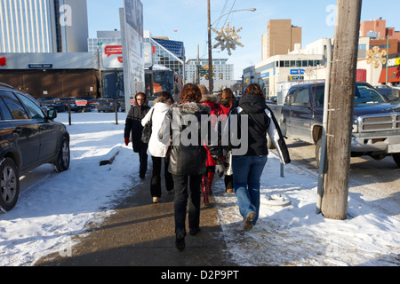 women wearing winter clothing walking along cold snow covered downtown street Saskatoon Saskatchewan Canada Foto Stock