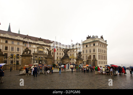 I turisti con ombrelloni si riuniscono all'ingresso del castello di Praga in una giornata di pioggia, esplorando lo storico quartiere di Hradčany nel cuore della città. Foto Stock