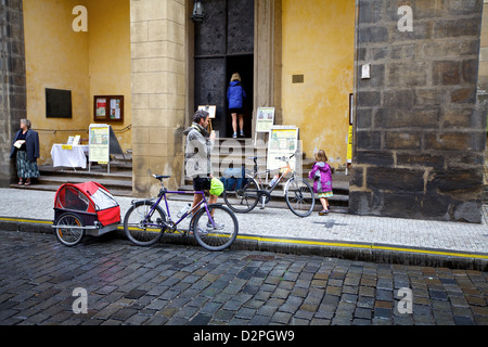 Una famiglia fa una pausa all'esterno di un edificio storico su una strada acciottolata a Praga, con biciclette e un rimorchio per bambini che riflette la miscela di storia della città Foto Stock