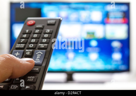 Telecomando per la TV cambia i canali il pollice sul blu sullo schermo TV Foto Stock