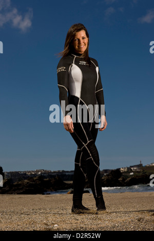 Surfista femmina permanente sulla spiaggia in wetsuit, sorridente