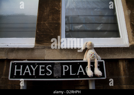 Un perse o abbandonate del bambino giocattolo di coniglio siede su un cartello stradale a Hayes Place, bagno, Somerset Foto Stock