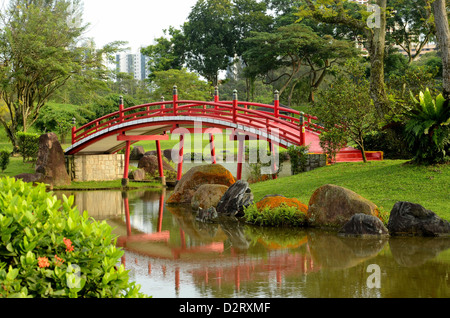 Pittoresca rosso curvo in stile Giapponese ponte sul torrente in Giardini Giapponesi, Singapore. Nota increspature e coperte di muschio di massi. Foto Stock