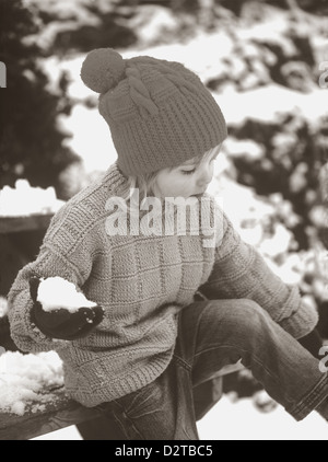 Foto in stile vintage di giovane ragazza che indossa un ponticello e un cappello in stile vintage, tenendo una palla di neve in inverno in Cornovaglia, Inghilterra, Regno Unito Foto Stock