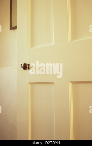 Dettaglio del vecchio interno con pannelli in legno porta dipinta di bianco con manopola in ottone aperta permanente per rivelare la parete con specchio Foto Stock