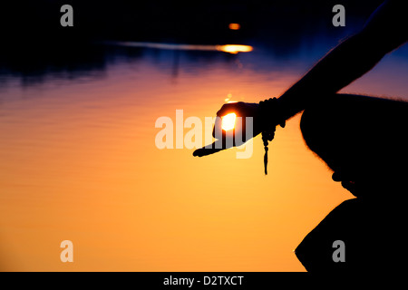 Sunrise silhouette di una mano mans mentre medita sulle rocce in un lago indiano. Andhra Pradesh, India Foto Stock