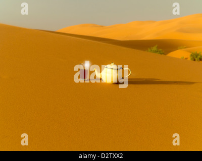 Bicchiere di tè e smalto teiera gettando ombra sulle dune di sabbia nel deserto di Erg Chebbi vicino a dune di Merzouga, Marocco, Africa del Nord Foto Stock