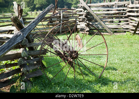 Split cancellata con un vecchio arrugginito tosaerba di fieno in piedi contro di essa in un prato, campo verde di boschi in background Foto Stock