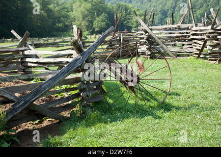 Split cancellata con un vecchio arrugginito tosaerba di fieno in piedi contro di essa in un prato, campo verde di boschi in background Foto Stock